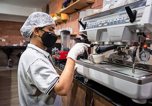 A barista in a café prepares coffee, ideal for visitors enjoying adventure games and mystery rooms in Banjara Hills, Hyderabad.