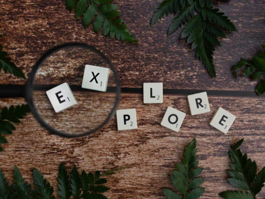 Magnifying glass over tiles spelling "EXPLORE," surrounded by ferns, symbolizing puzzle solving adventures at escape room Hyderabad.