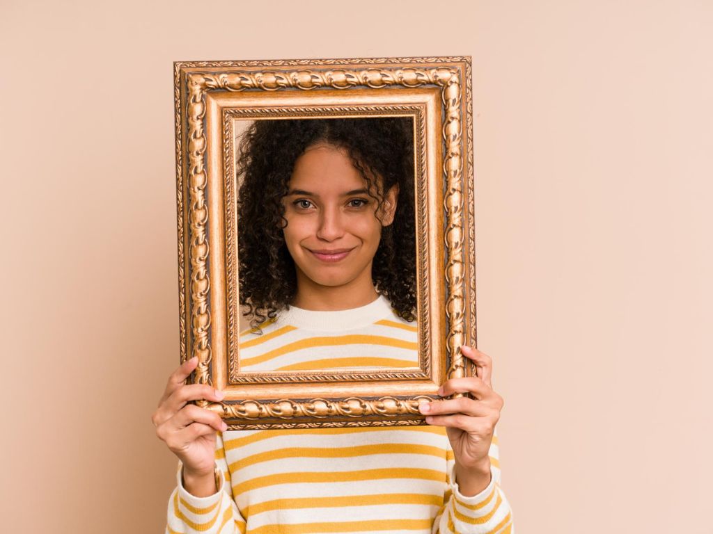 Woman holding a decorative gold photo frame in front of her face, representing personalised rakhi gift ideas like custom photo frames in Hyderabad from Lock N Escape