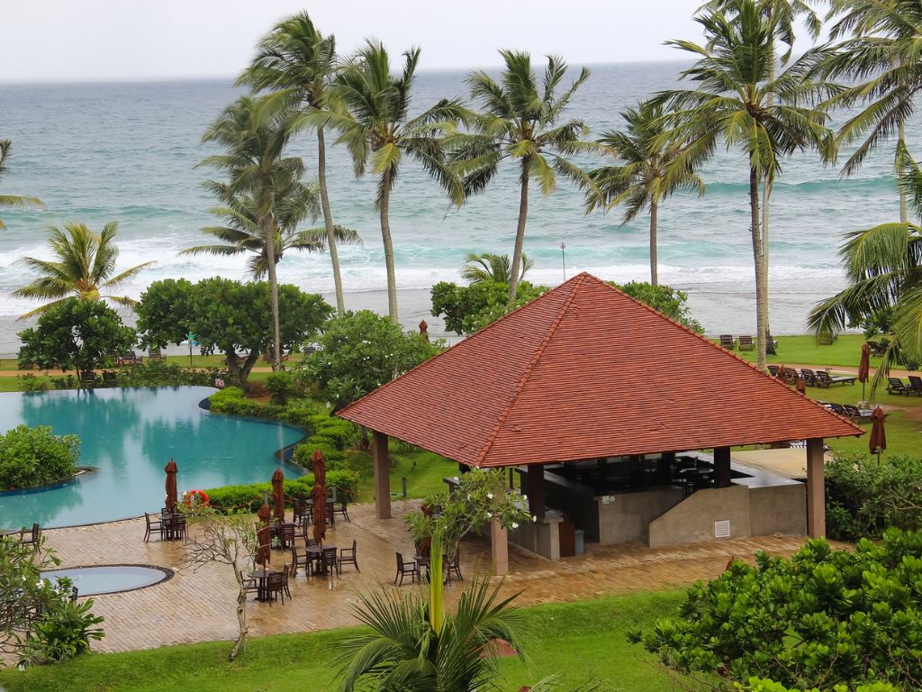 Resorts & Retreats for Day Outings or Overnight Offsites — lush resort with a pool, pavilion, and palm trees overlooking the sea, representing premium corporate retreat venues near Hyderabad